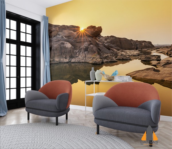 Sunset over a rocky river landscape as a wall mural in a modern living room with two chairs.