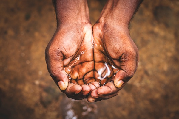 Close-up of cupped dark-skinned hands holding clear water, showcasing the intricate lines of the palms.