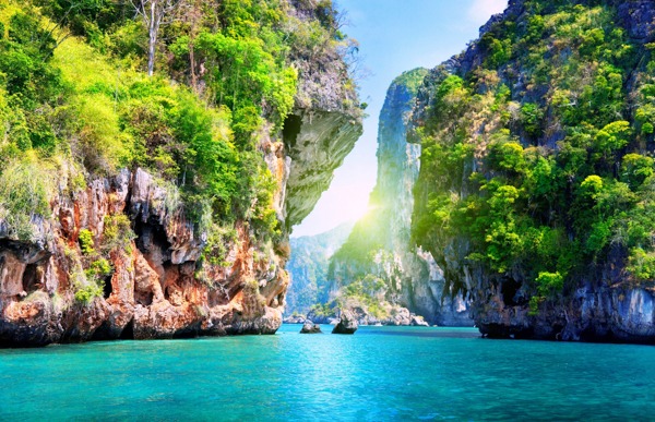 Deep blue ocean winding between large, green, rocky cliffs under a sunny sky.